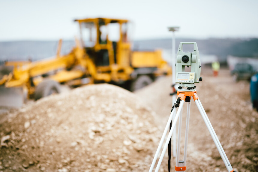 Surveying device on construction site with yellow bulldozer in the background.