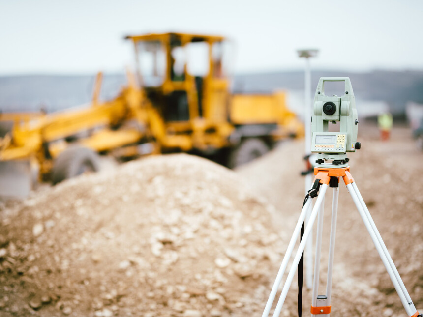 Vermessungsgerät auf Baustelle mit gelbem Planierraupenfahrzeug im Hintergrund.