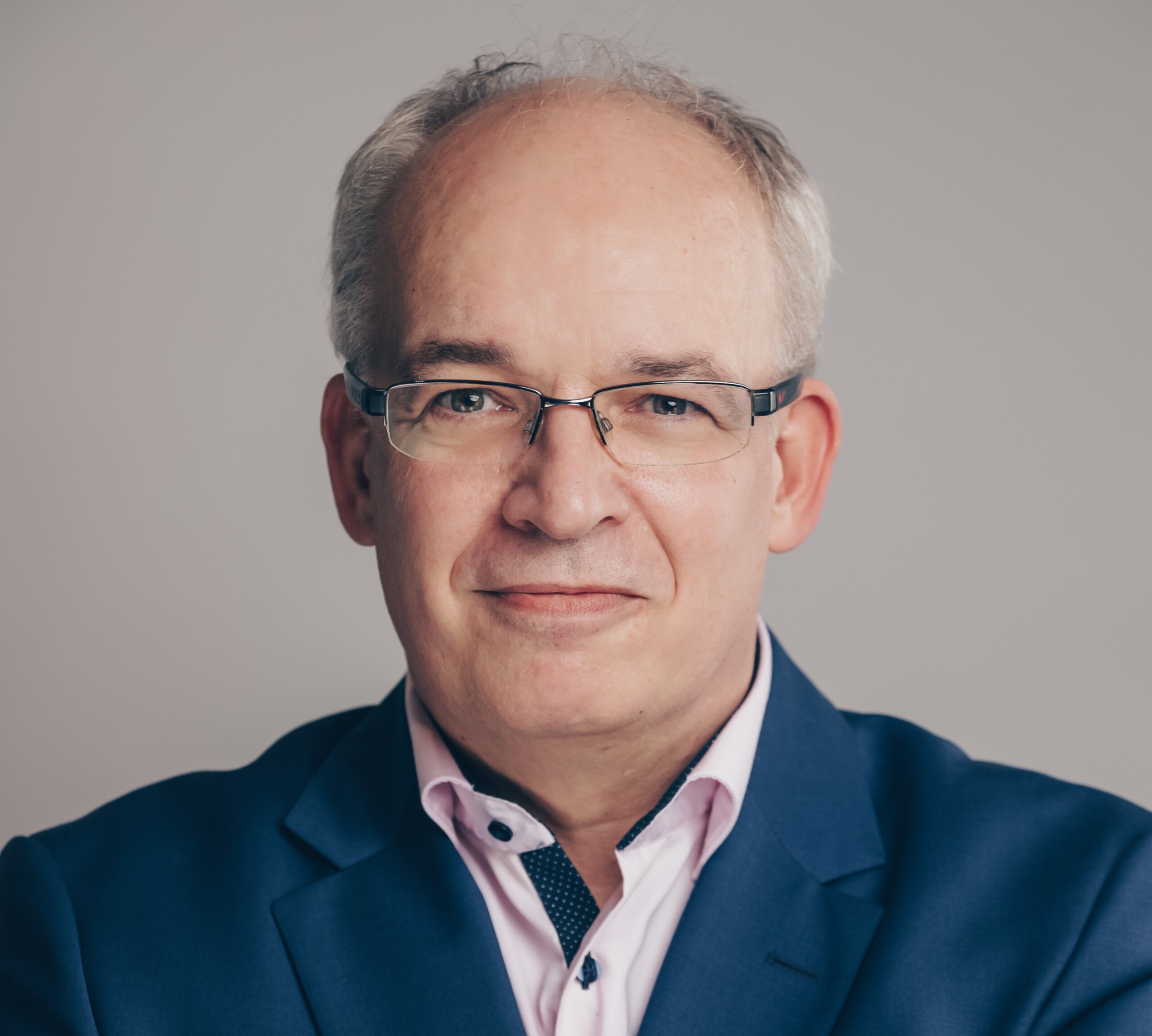 Portrait of Michael Berlemann with glasses, blue suit and pink shirt