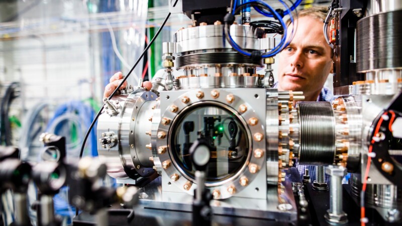 Wissenschaftler arbeitet an komplexem Vakuumgerät mit zahlreichen Kabeln und Metallteilen im Labor.