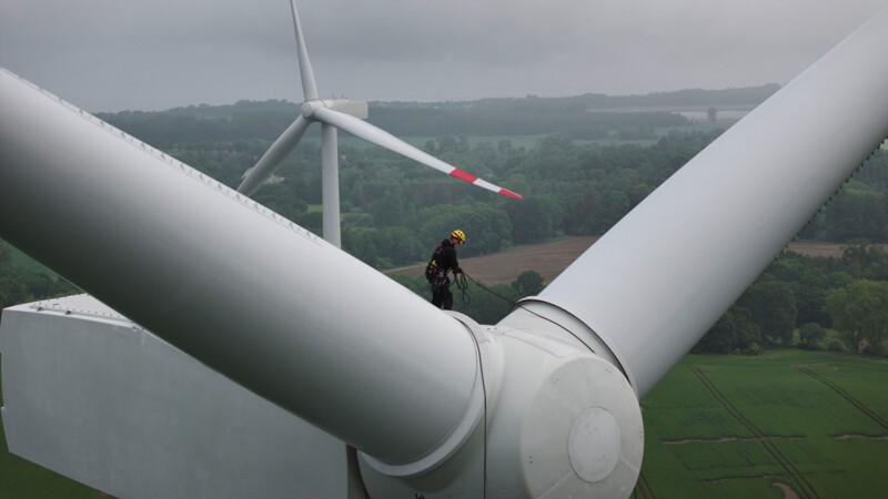 Ein Arbeiter hoch oben zwischen den Rotorenblättern eines Windrades