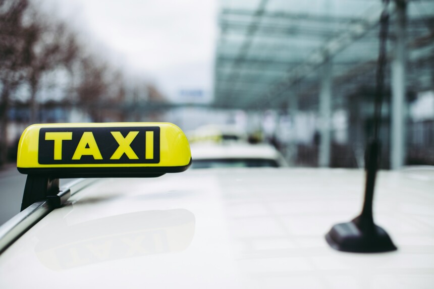 Gelbes Taxi-Schild auf dem Dach eines weißen Taxis mit unscharfem Hintergrund.