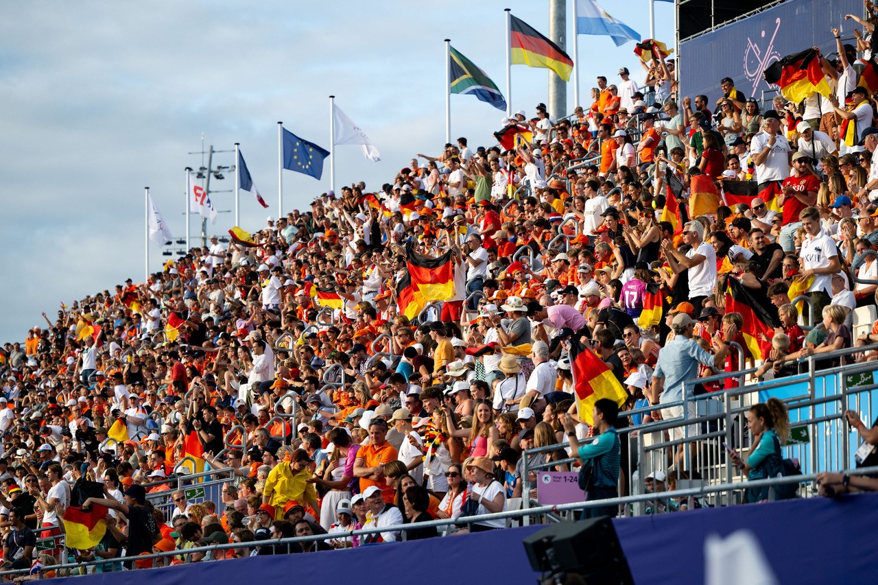 Große jubelnde Menschenmenge mit vielen deutschen Flaggen in einem Stadion bei Tageslicht.