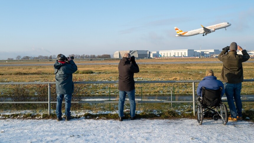 Besucherinnen und Besucher beobachten ein aufsteigendes Flugzeug im Gewerbegebiet Finkenwerder
