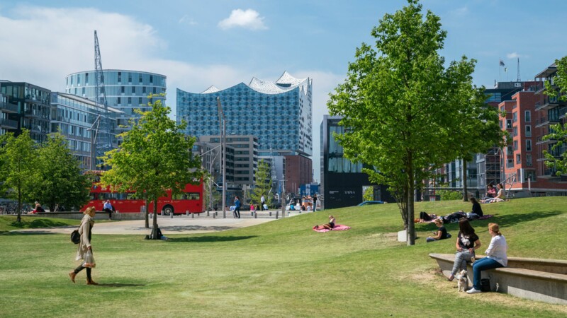 Menschen entspannen sich in einem Park mit Blick auf die moderne Elbphilharmonie in Hamburg.