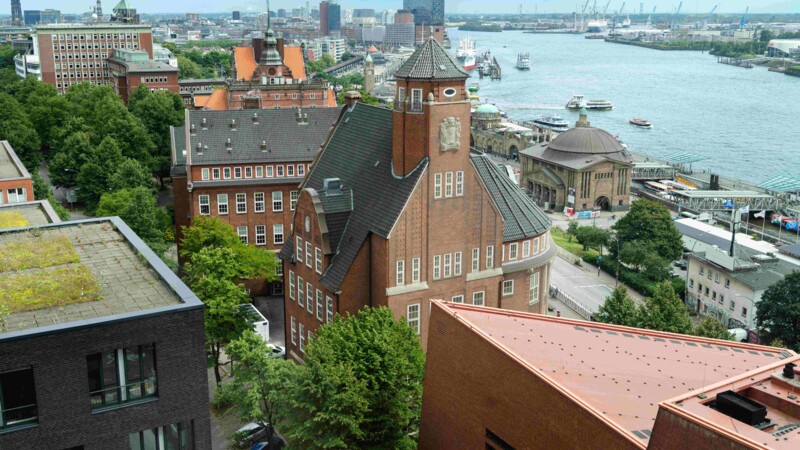 Blick auf Hamburger Hafen mit historischen und modernen Gebäuden, darunter der Schumacher-Bau des BNITM, sowie Elbe und Schiffen.