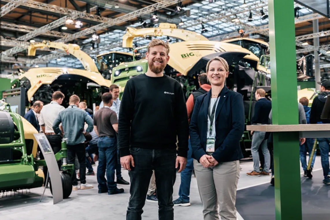 Two people standing in front of farming machinery at a trade fair