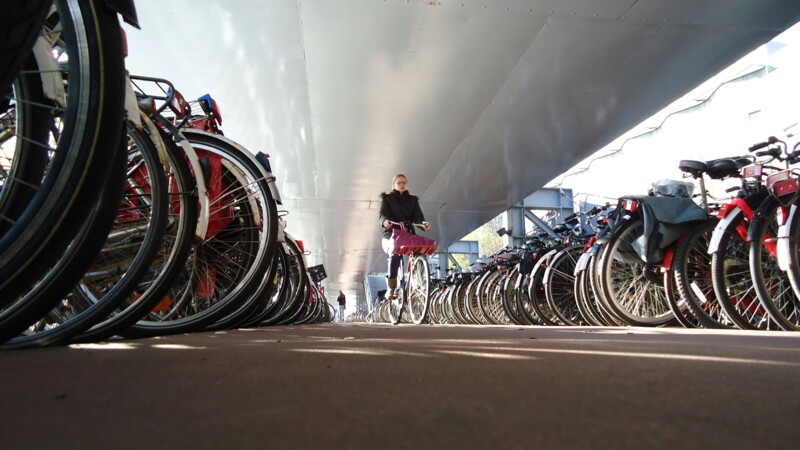 Fahrradfahrerin fährt unter einer Brücke an vielen Fahrrädern vorbei