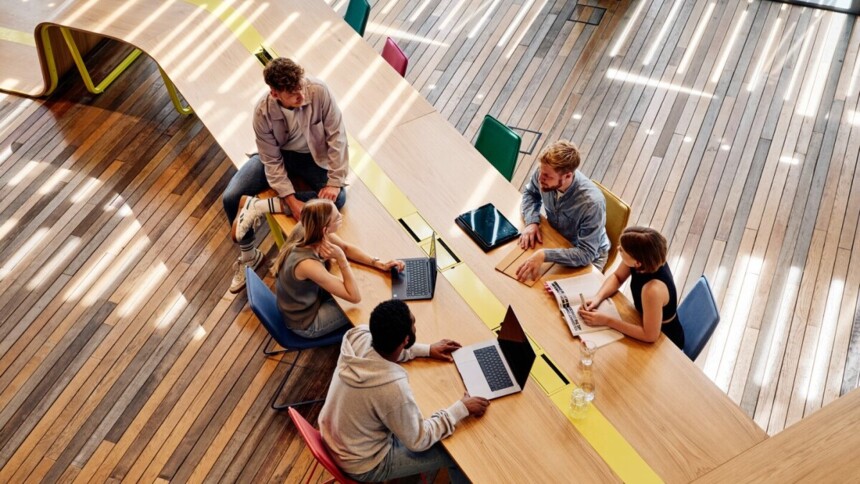 Branchenservice New Work & New Services: Fünf Menschen bei einem Meeting mit Laptops an einem langen Tisch