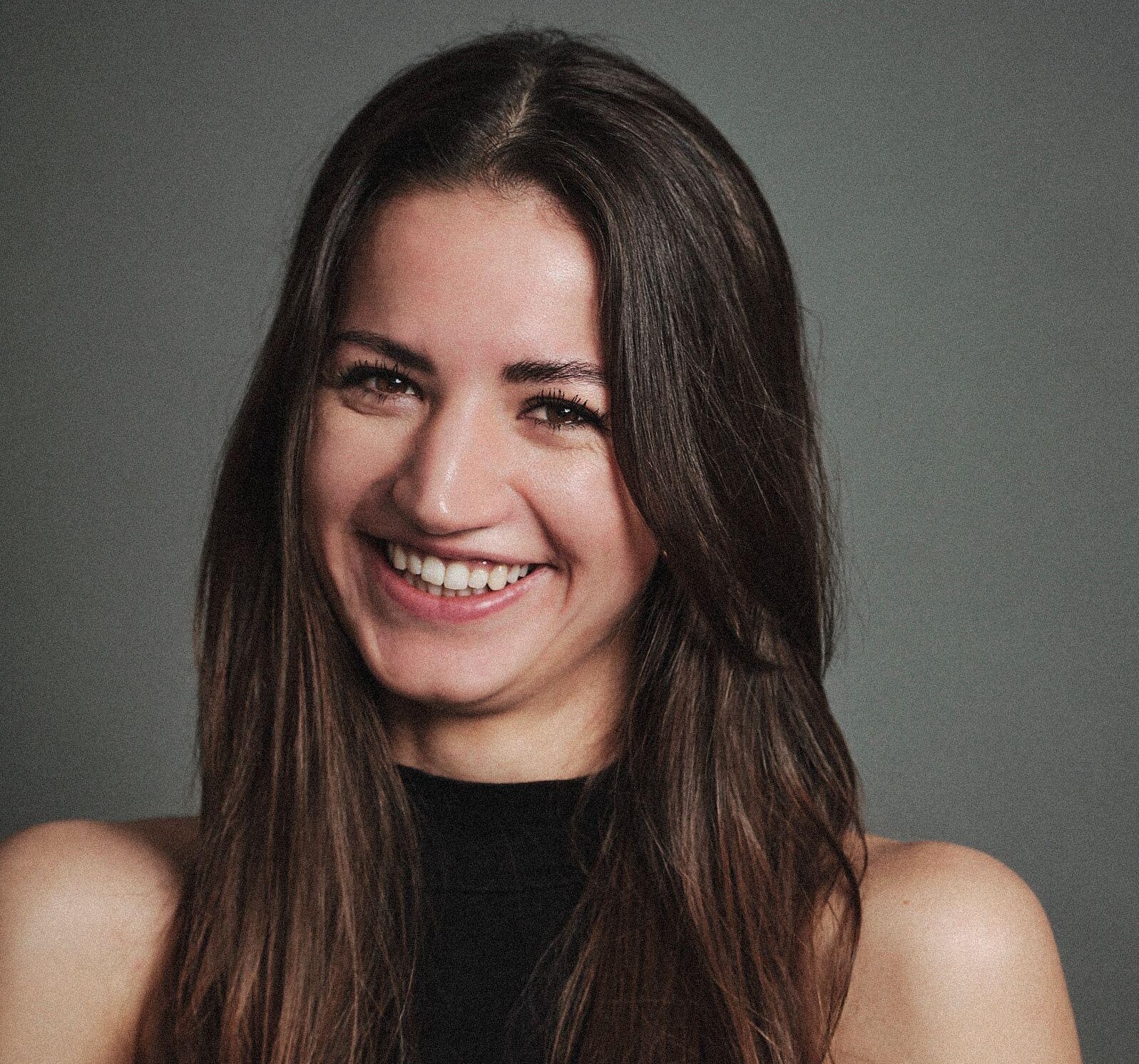 Young brunette smiling in front of a grey wall