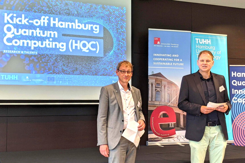 Zwei Männer stehen bei der Kick-off-Veranstaltung Hamburg Quantum Computing vor Präsentationsbild und Bannern.