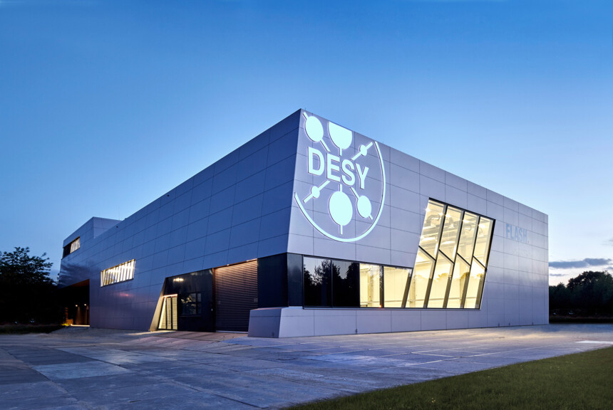Modern DESY research building with illuminated logo at dusk.
