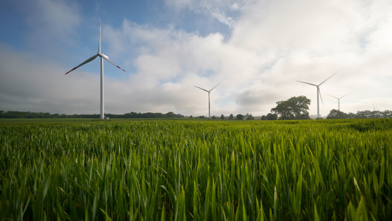 Windräder stehen auf einem grünen Feld unter einem bewölkten Himmel.