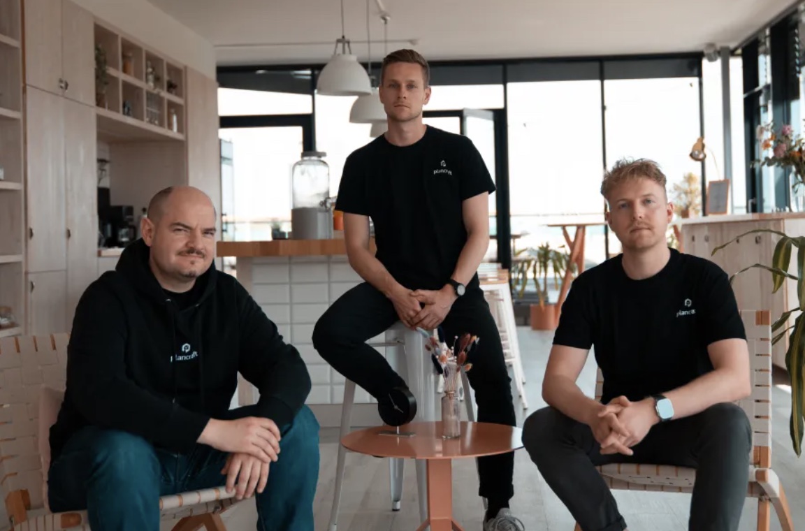 Drei Männer in schwarzer Firmenkleidung sitzen in modern eingerichteter Lounge mit großen Fenstern.