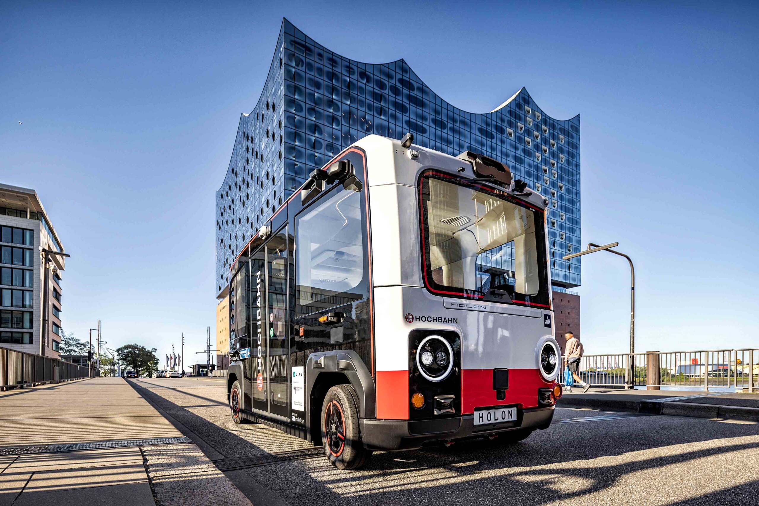 Kleiner autonomer Elektrobus vor der Elbphilharmonie in Hamburg bei sonnigem Wetter.