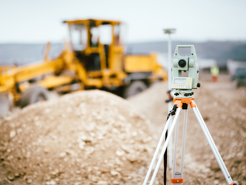 Vermessungsgerät auf Baustelle mit gelbem Planierraupenfahrzeug im Hintergrund.