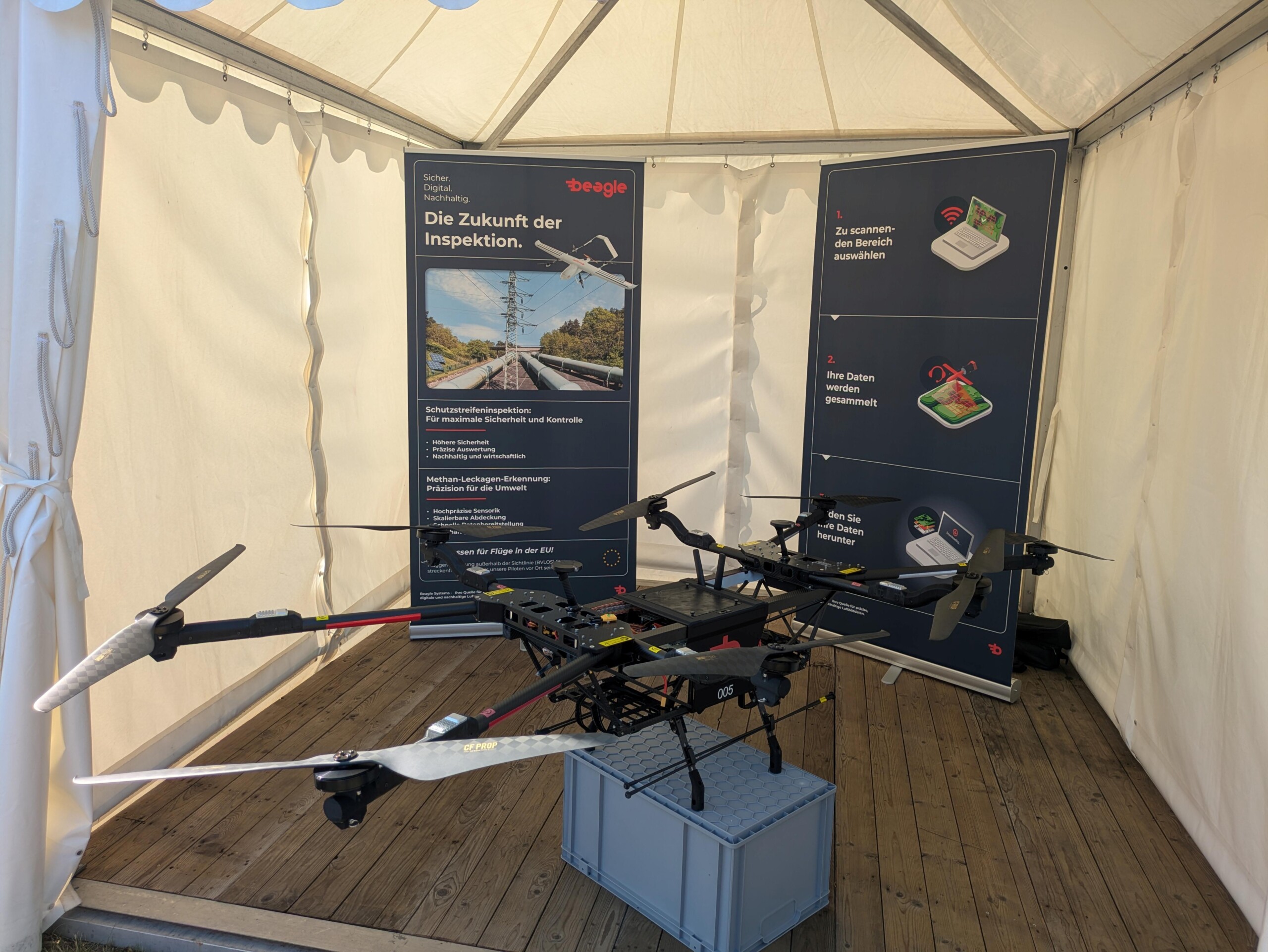 Large industrial drone displayed inside a tent with German informational posters about inspection technology.