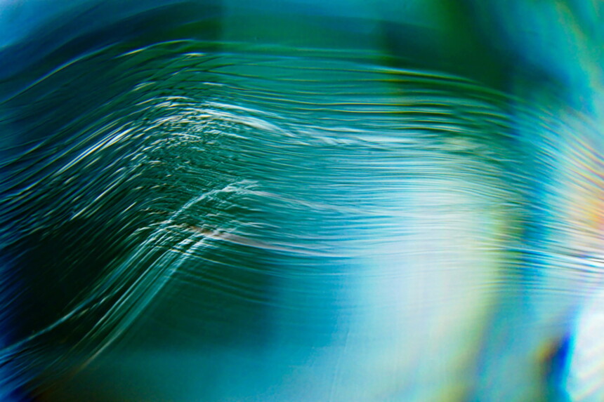 Nahaufnahme von Wellen und Lichtreflexionen auf der Wasseroberfläche in Blau- und Grüntönen.