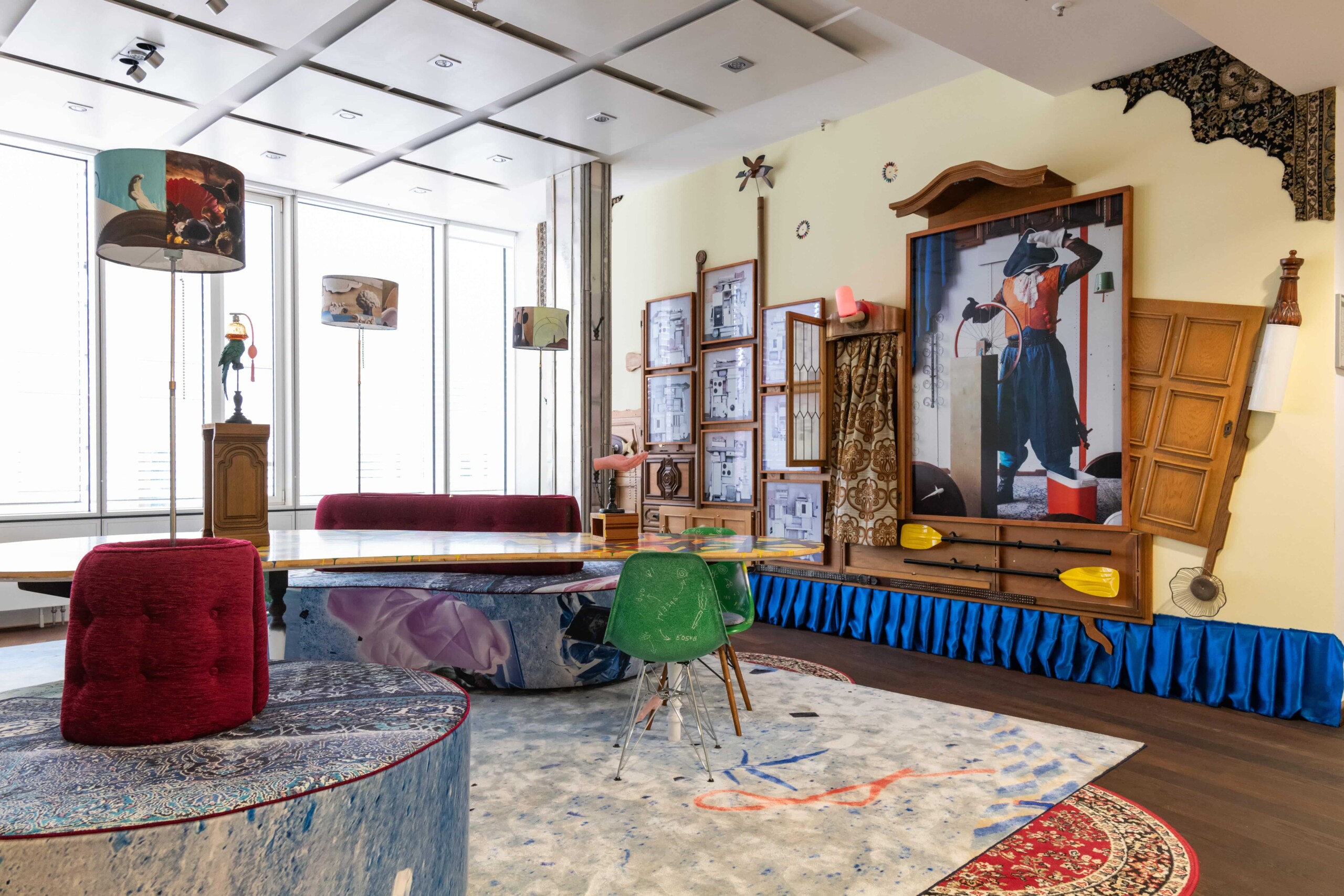 Bunt eingerichteter Raum mit ungewöhnlichen Möbeln, Lampen und großem Kunstwerk an der Wand.