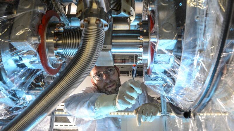 Wissenschaftler mit Handschuhen arbeitet konzentriert an komplexer technischer Apparatur in Laborumgebung.