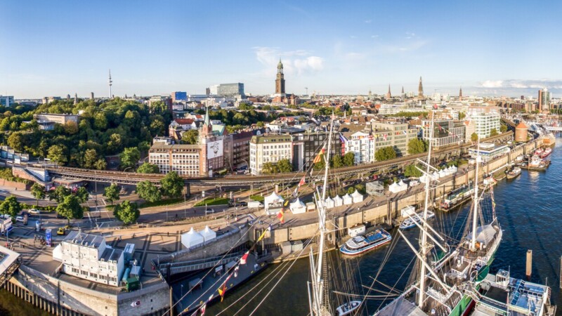 Panoramic view of Hamburg harbour with historic ships, waterfront buildings, and city skyline under a clear sky.