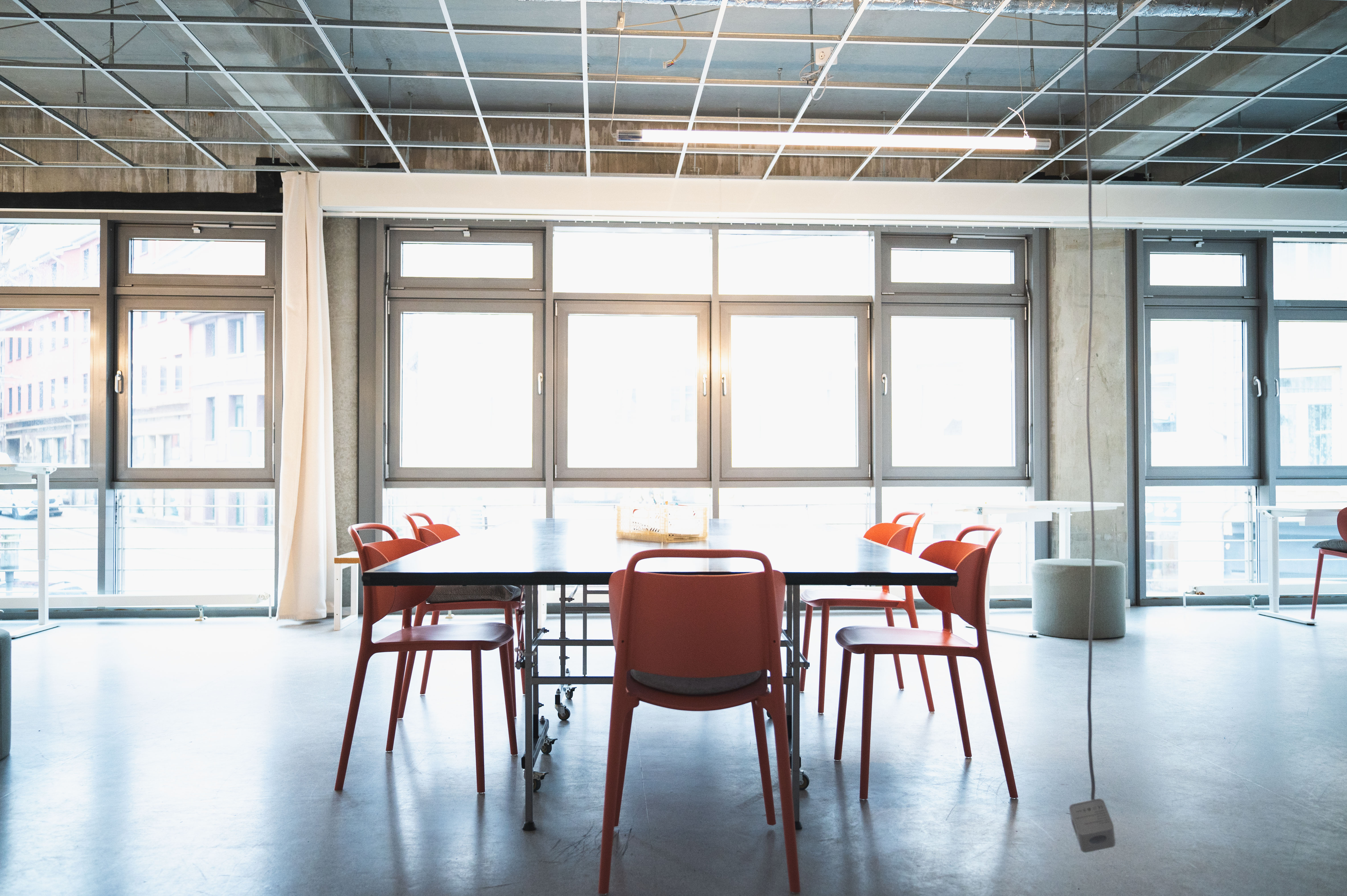 Arbeitsplatz im Co-Working-Café, großer Tisch mit fünf Stühlen vor einer Fensterfront