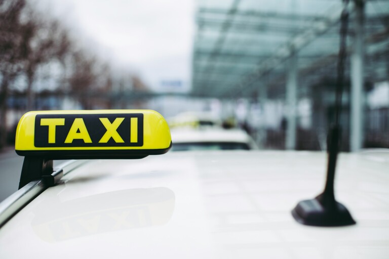 Gelbes TAXI-Schild auf dem Dach eines weißen Taxis mit unscharfem Hintergrund.