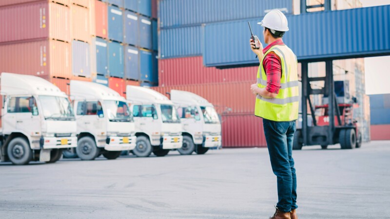 Ein Mann in gelber Warnweste kooridiniert LKW-Transporte von Containern