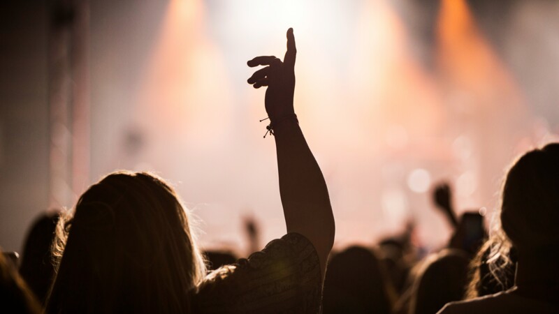 Silhouette einer Person mit erhobener Hand bei einem Konzert vor hellen Bühnenlichtern