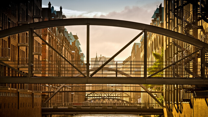 Blick auf mehrere Brücken und historische Backsteingebäude in der Speicherstadt bei Sonnenuntergang.