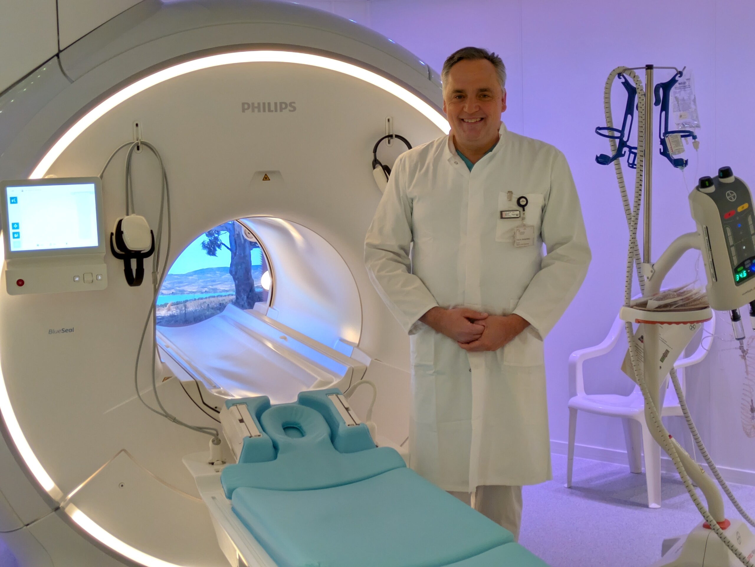 Professor Christoph Weber stands beside an MRI scanner in consultation room