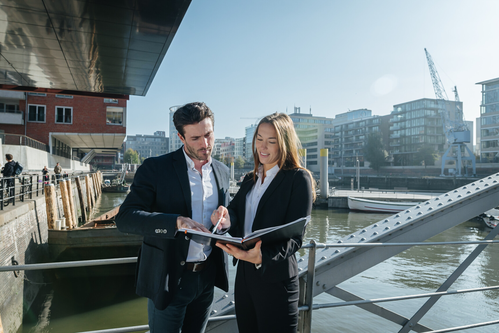 Two business professionals discussing documents by a riverside with modern buildings in the background.