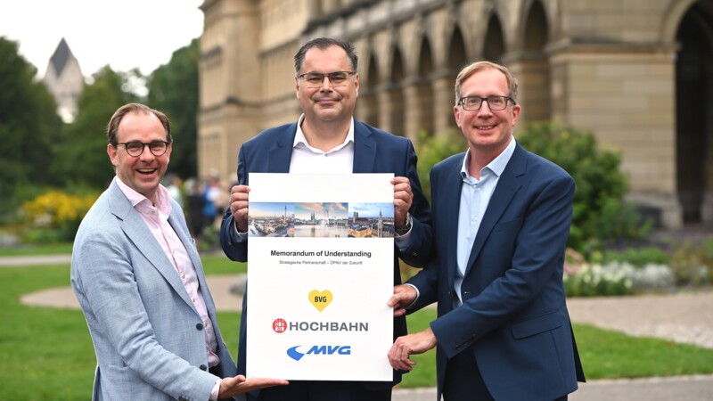 Drei Männer präsentieren ein Memorandum of Understanding zwischen BVG, Hochbahn und MVG im Freien.
