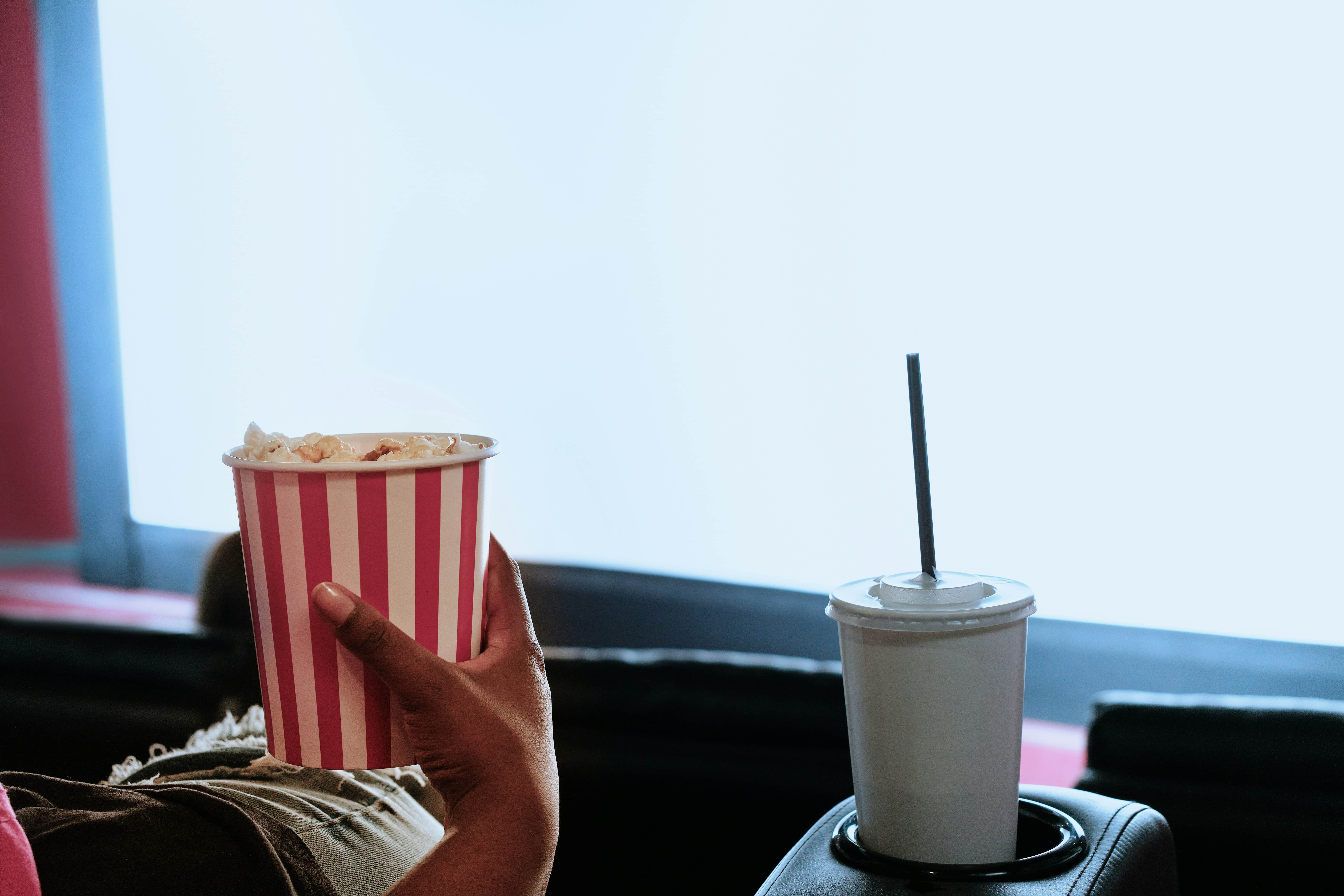 Frau im Kino, die einen Becher Popcorn in der Hand hält, daneben ein Becher mit Strohhalm, im Vordergrund sieht man die Kinoleinwand, Symbolbild Kino-Kongress