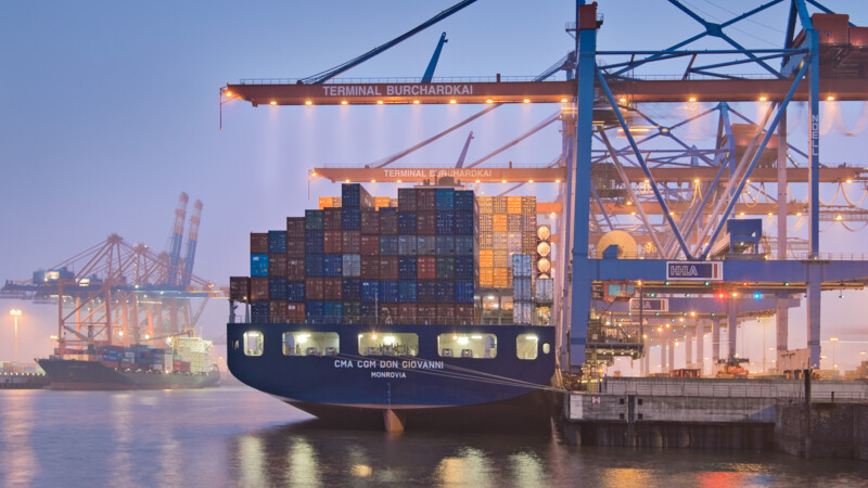 Container ship CMA CGM Don Giovanni docked at Terminal Burchardkai with cranes unloading cargo at dusk.