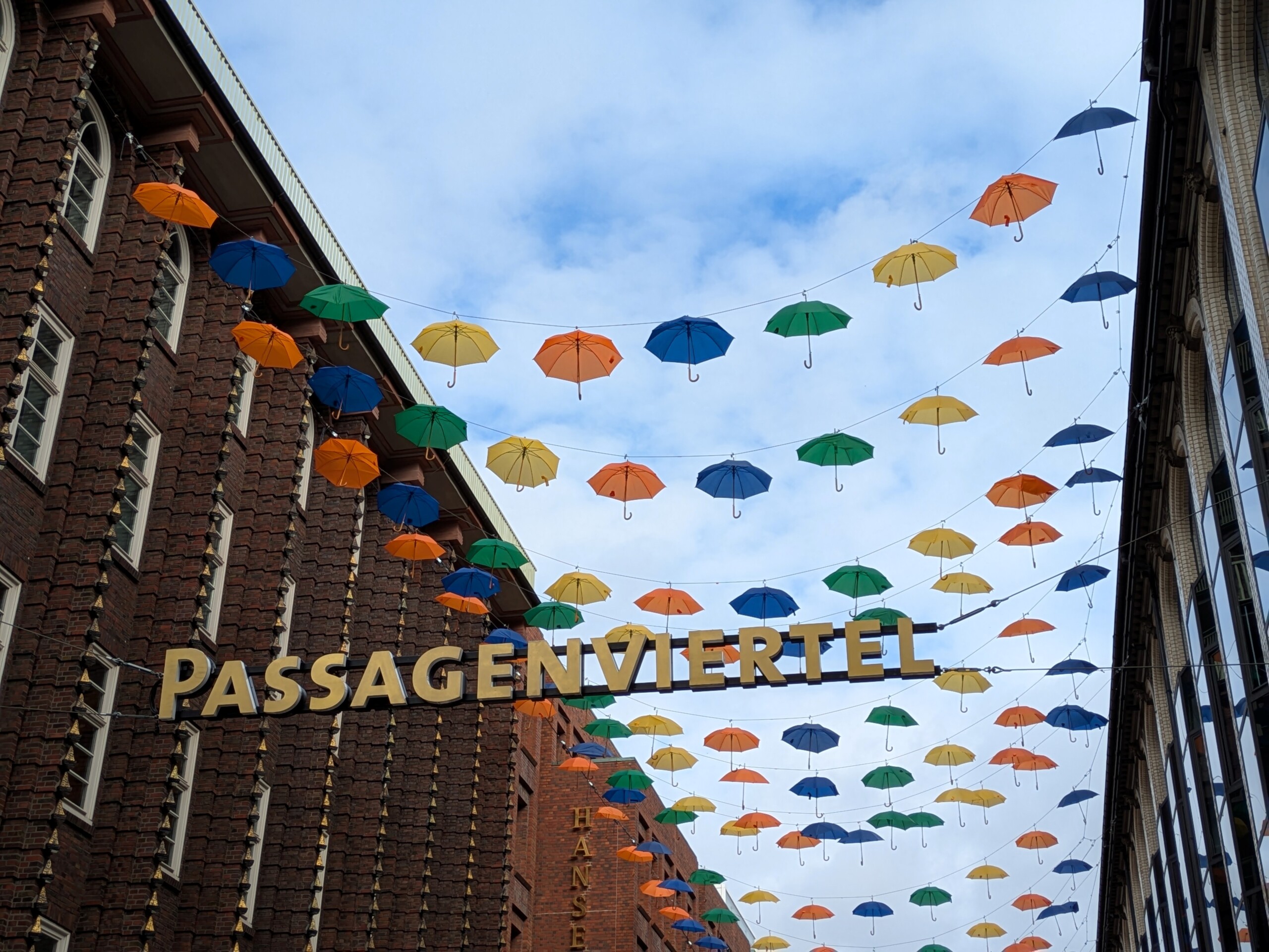 Bunte Regenschirme hängen über der Straße im Passagenviertel zwischen historischen Backsteingebäuden.