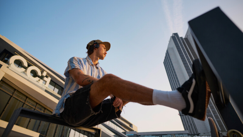 Youth with headphones and skateboard sits on a bench outside the Congress Center Hamburg