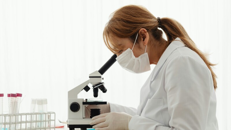 Scientist in a lab examines a sample through a microscope 