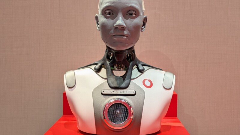 Büste eines humanoiden Roboters mit Gesicht und technischem Oberkörper auf rotem Podest.