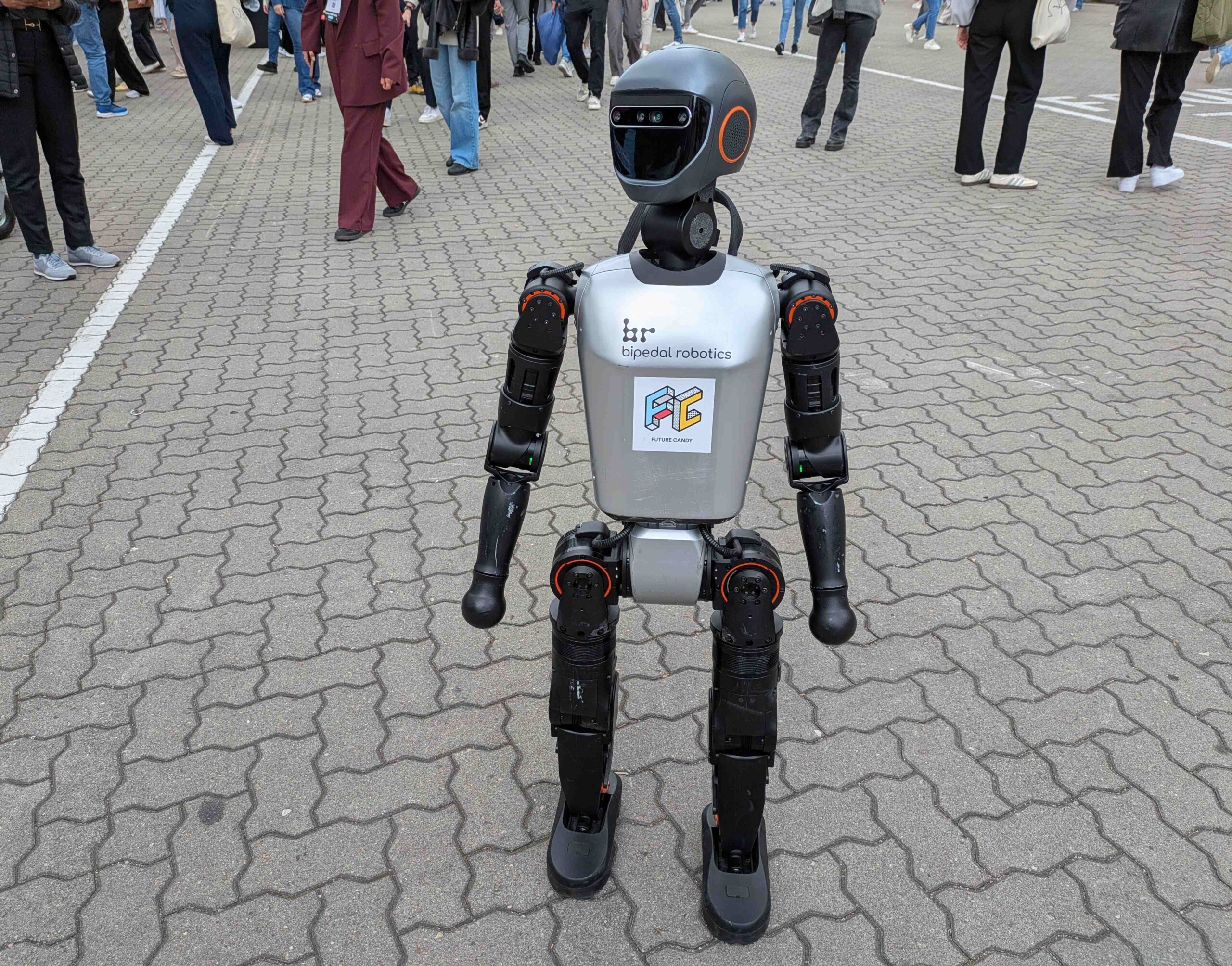 Humanoid robot stands on a pavement in a crowd of people
