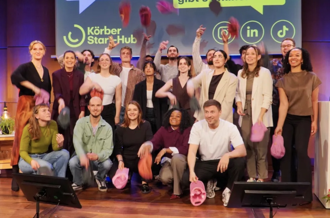 Gruppenfoto von jungen Menschen, die bunte Mützen in die Luft werfen, vor einer Körber Start-up Hub Präsentation.