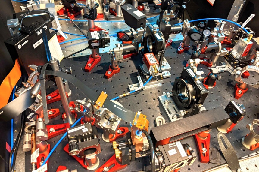 Optisches Labor mit Laser- und Linsensystemen auf einer perforierten Experimentierplatte.