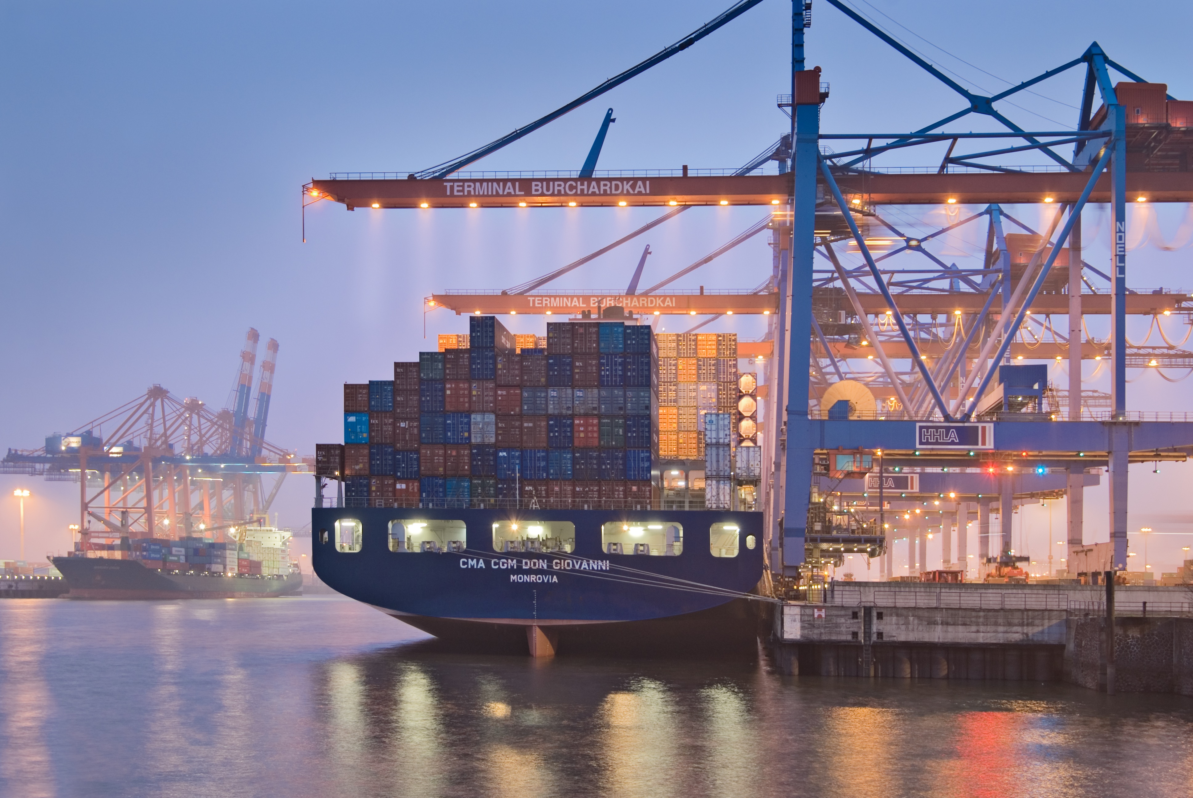 Container ship at the illuminated Burchardkai terminal in the port at dusk.