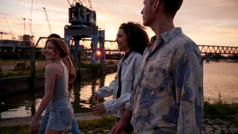 Symbolbild Universität und Zukunft: Vier junge Menschen spazieren bei Sonnenuntergang am Wasser entlang 