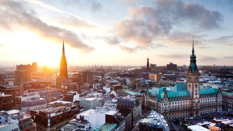 Blick auf Hamburg bei Sonnenuntergang mit Rathaus und Elbphilharmonie im Hintergrund.