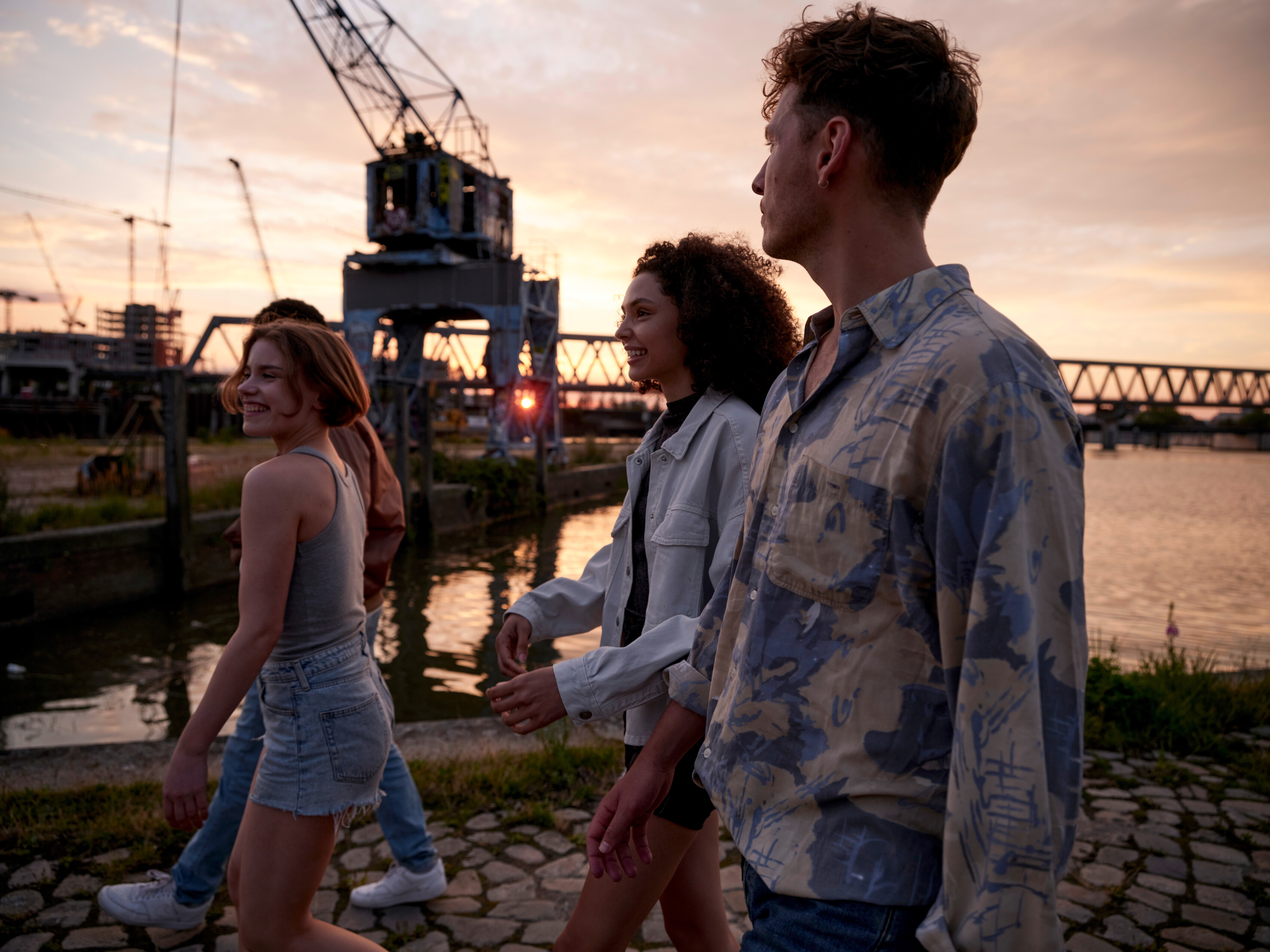 Symbolic image of the university and the future: four young people stroll along the water at sunset