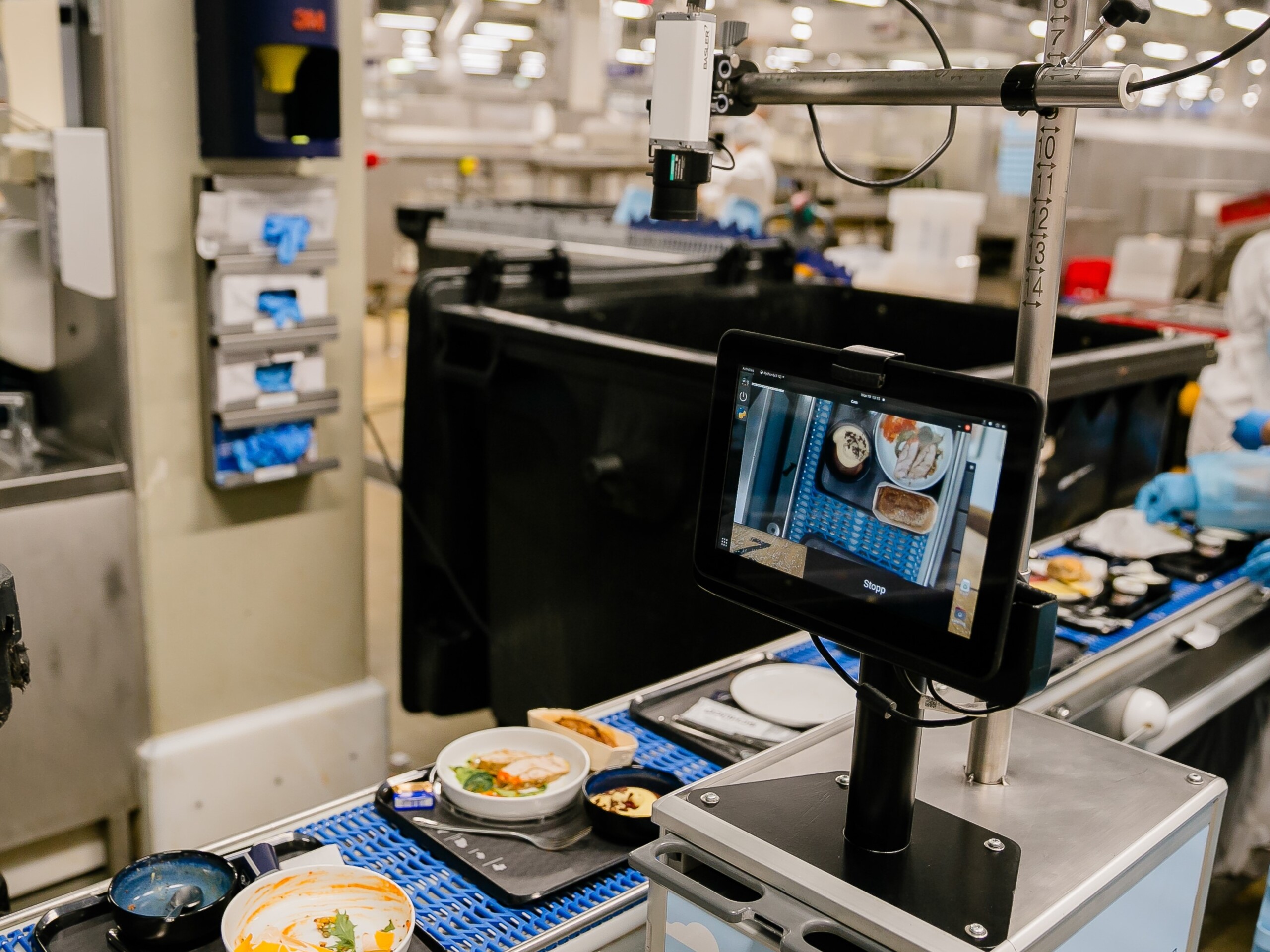 Tablet and camera monitors food trays on a conveyor belt in a factory 

