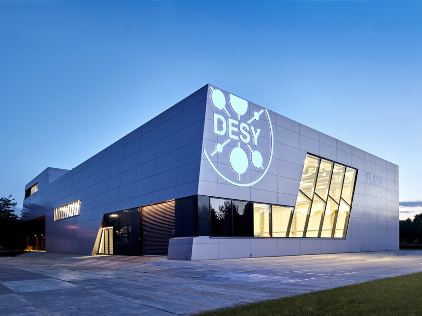 Modernes Forschungsgebäude des DESY mit beleuchtetem Logo bei Abenddämmerung.
