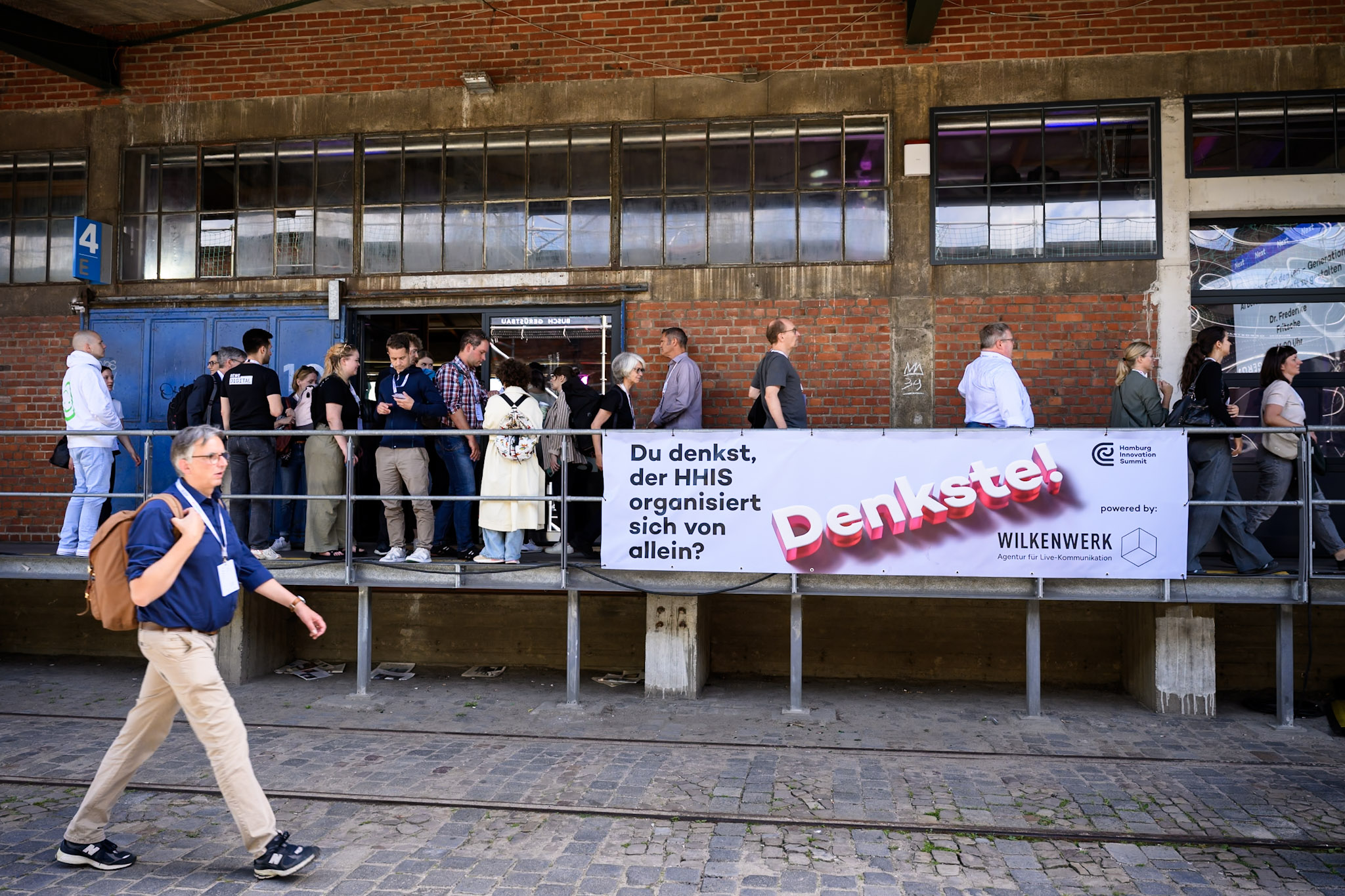 People queue in front of a brick building with a Hamburg Innovation Summit banner.