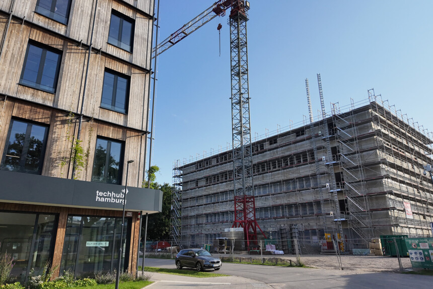 Construction crane and building site next to modern wooden building with sign "techhub hamburg" under a clear sky.